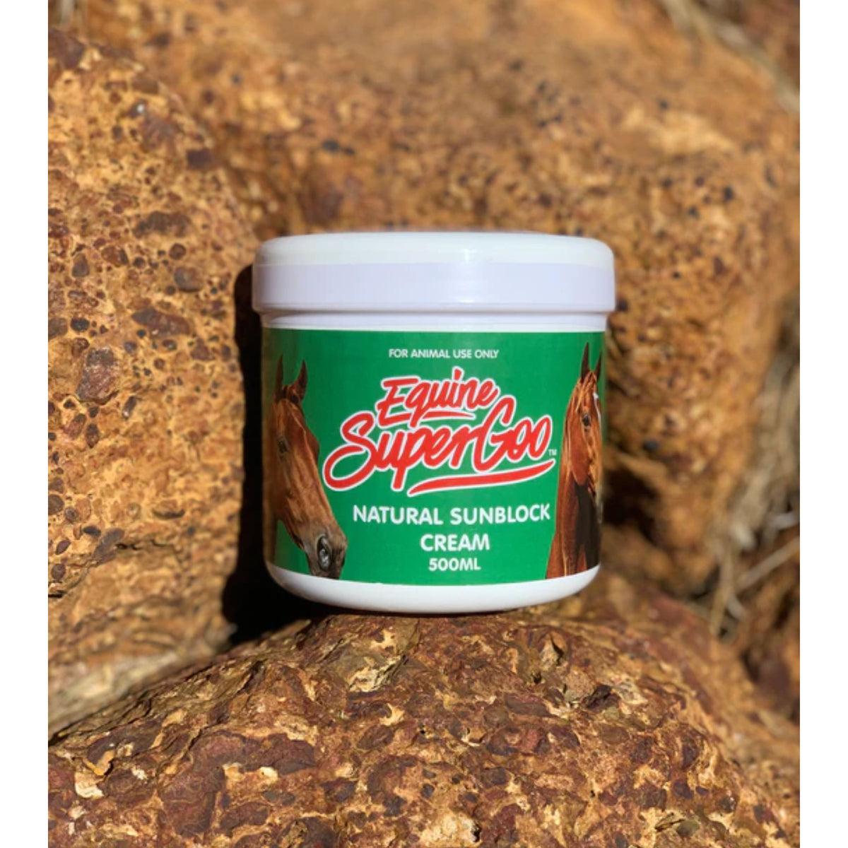 Tub of &quot;SuperGoo&quot; sunblock with green label, nestled in rocks.