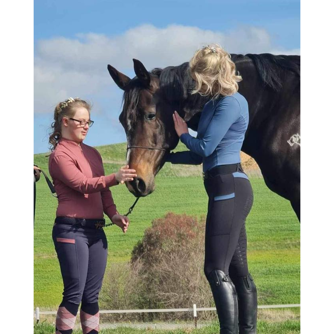 two ladies wearing equestrian clothing in pink and blue with a horse