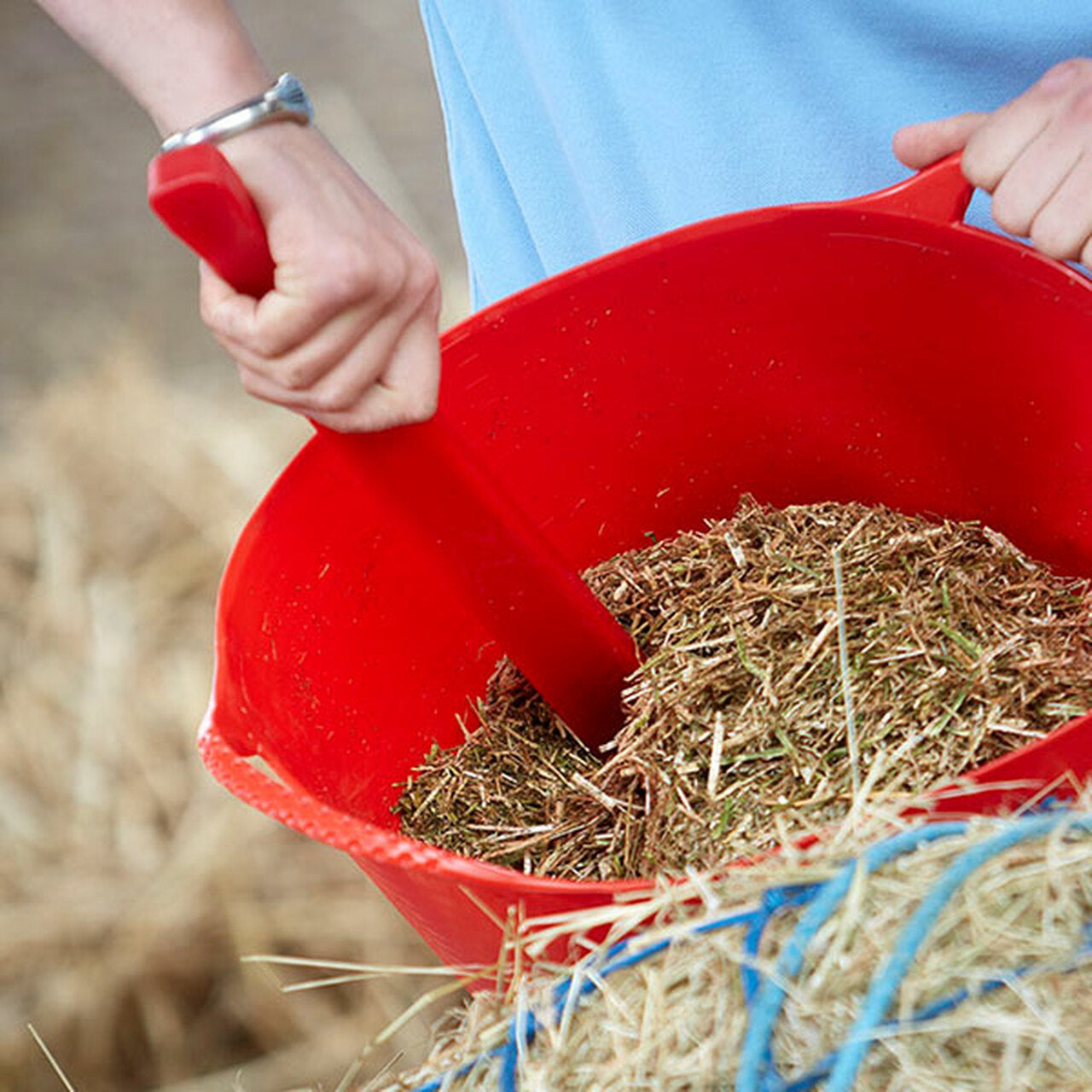 Hand using a red feed stirrer to stir chaff in a bucket.