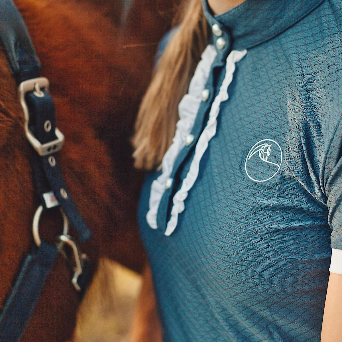 Close up of grey show shirt, with white frills, logo, and buttons.