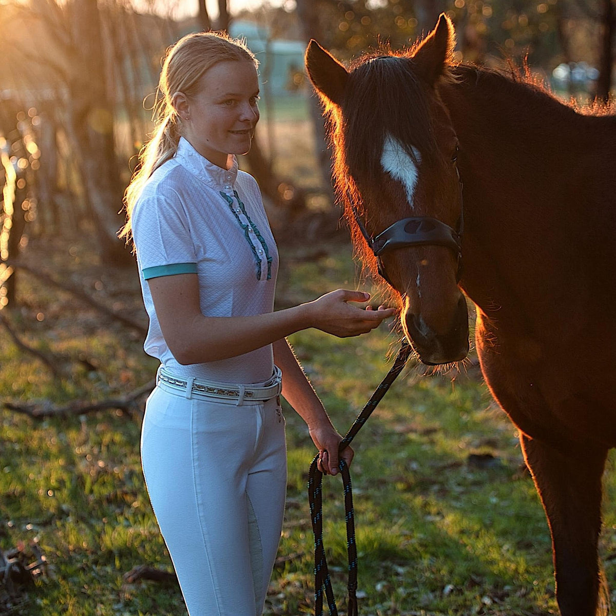 Lady holding horse, wearing white show shirt with turquoise cuffs and frills.
