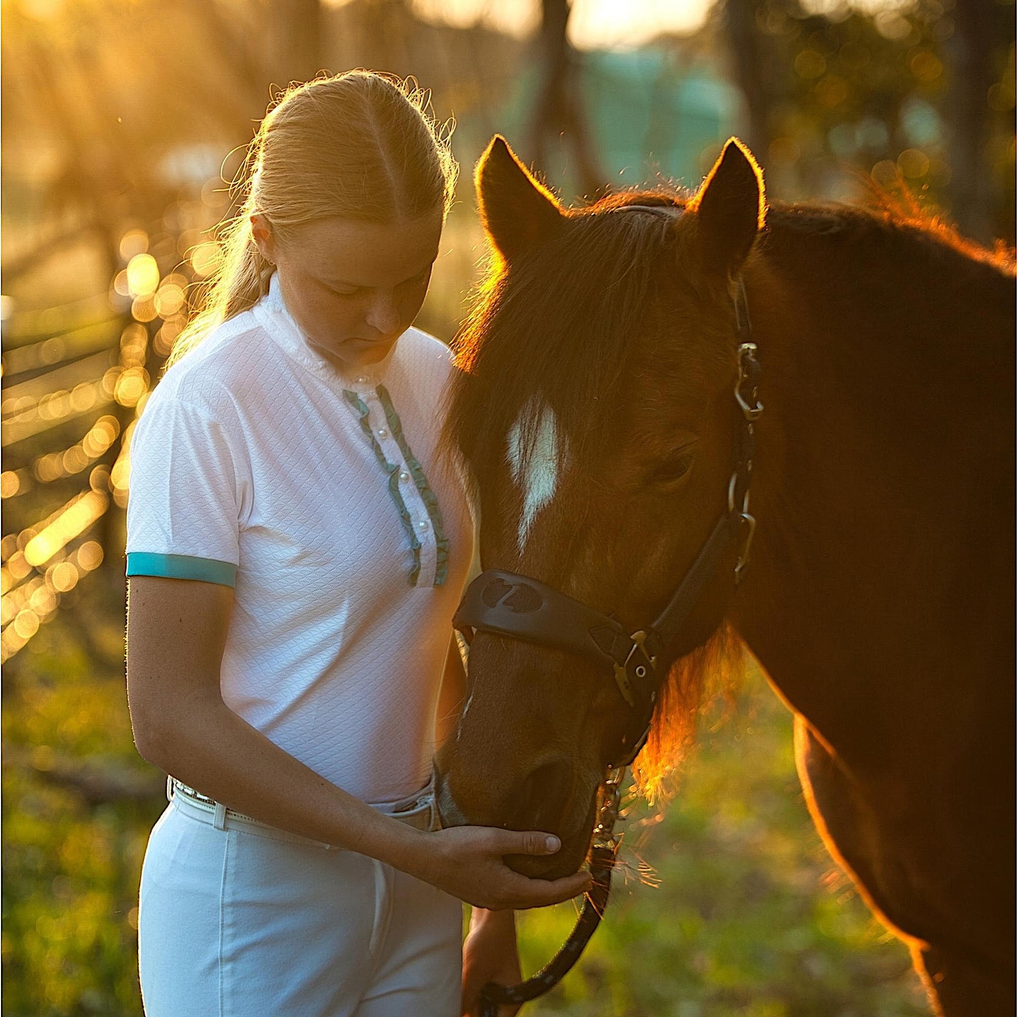 Lady holding a bay horse, wearing white show shirt with turquoise details.