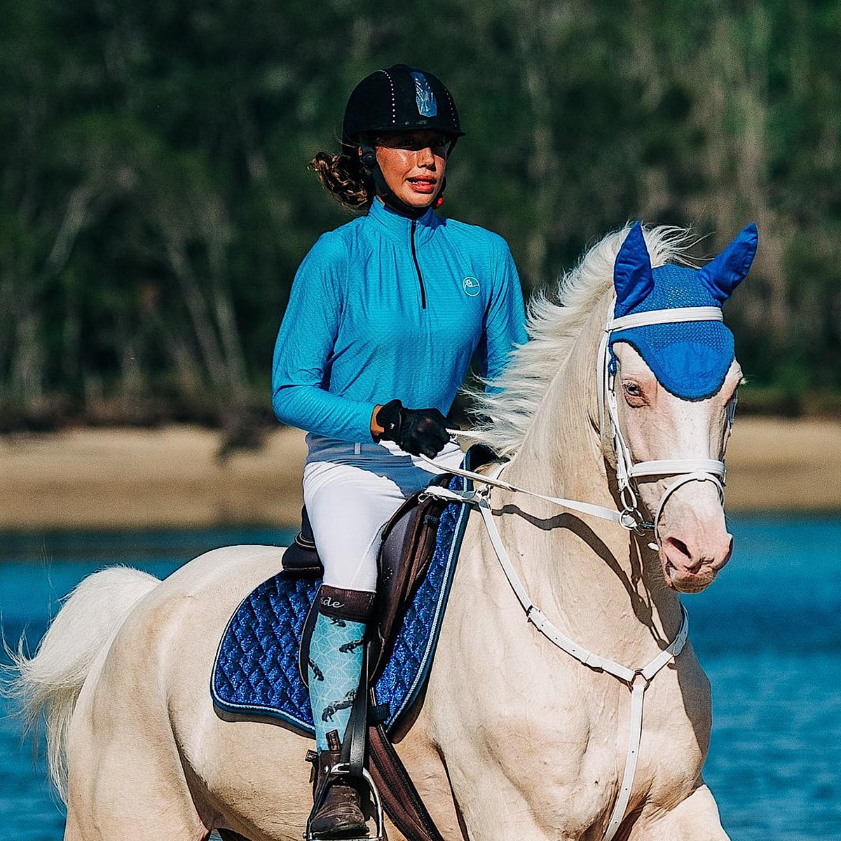 Cremello horse being ridden by rider in blue long sleeve shirt.