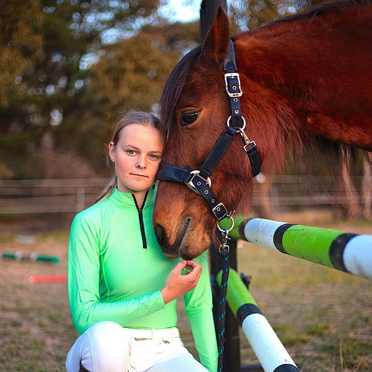 Lady kneeling beside a horse, wearing a green long sleeve shirt.
