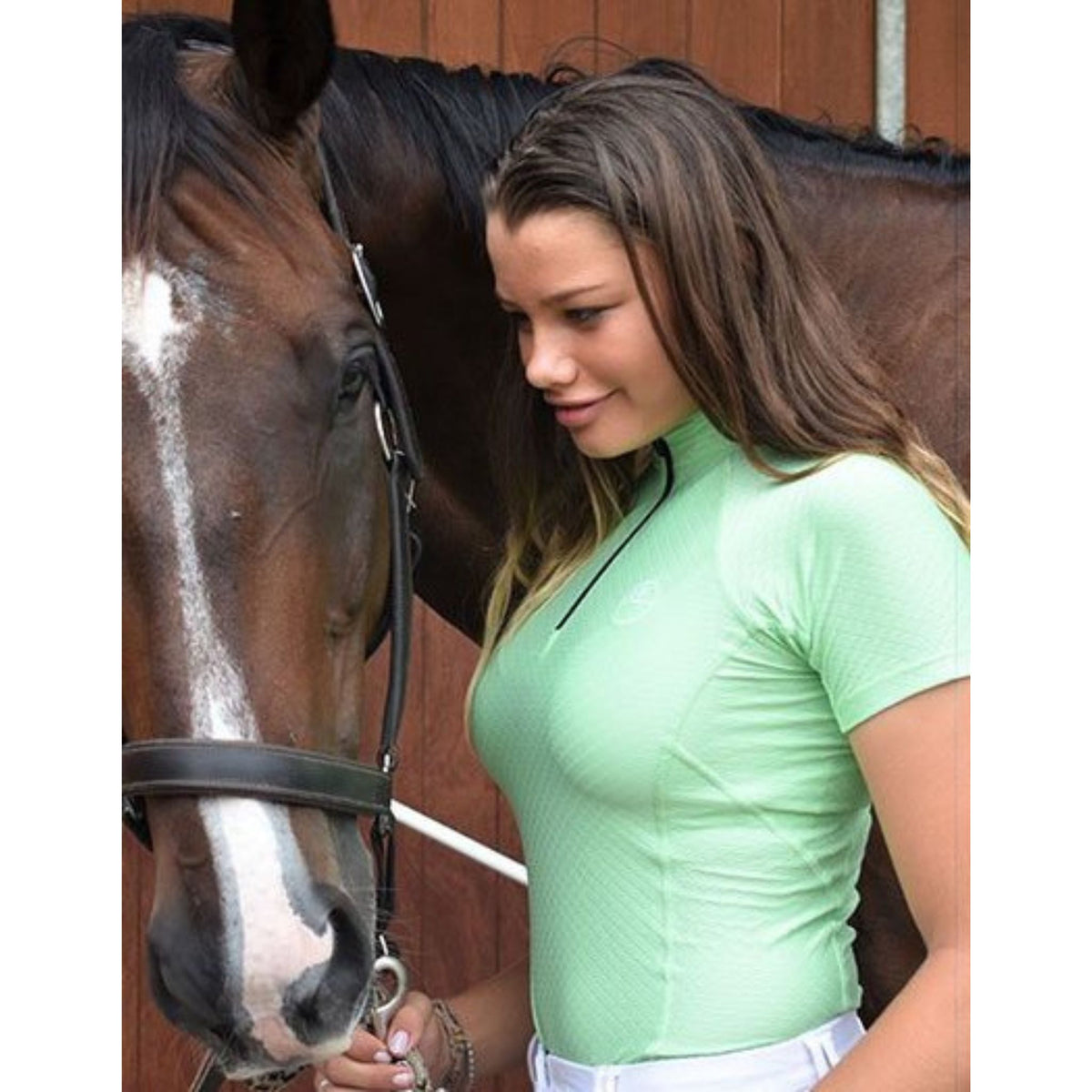 Lady holding bay horse, wearing short sleeve mint shirt with quarter zip.