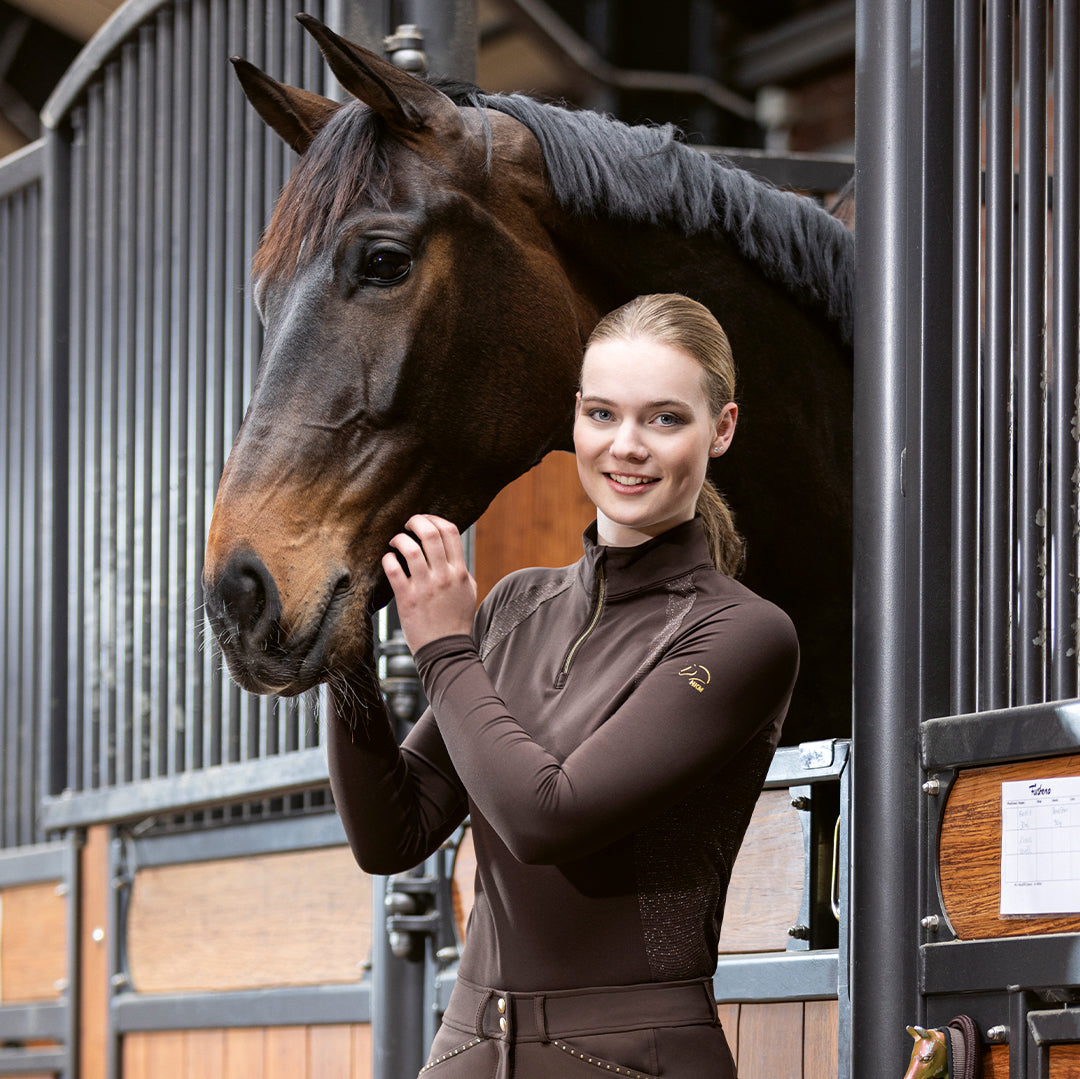 Girl wearing brown basil top standing next to horse.