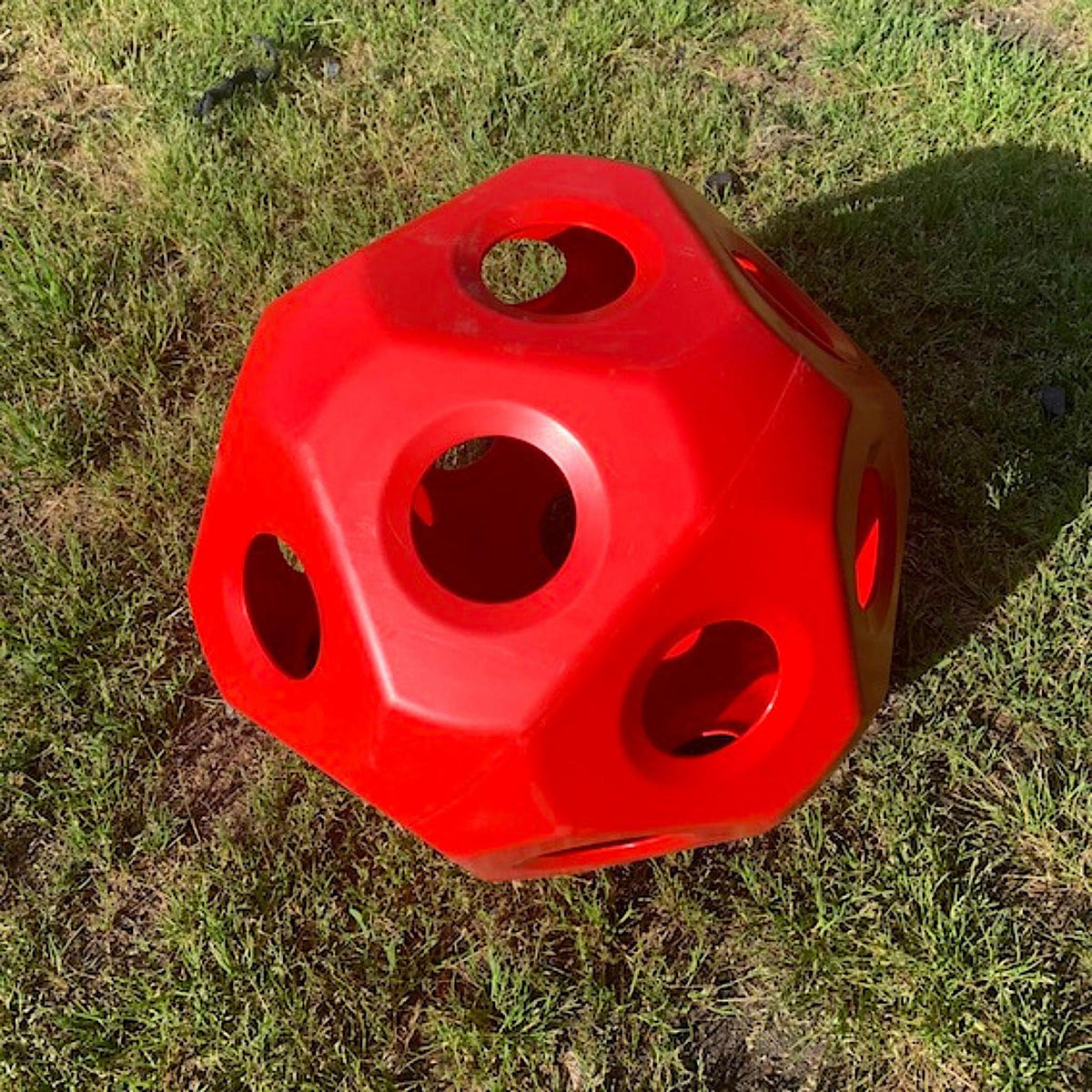 Red plastic hay ball with flat sides and moderately sized holes throughout.