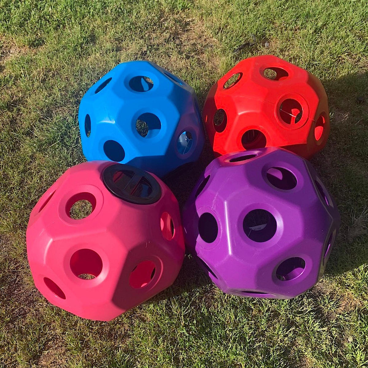 Four coloured hay balls of various colours sitting on grass.