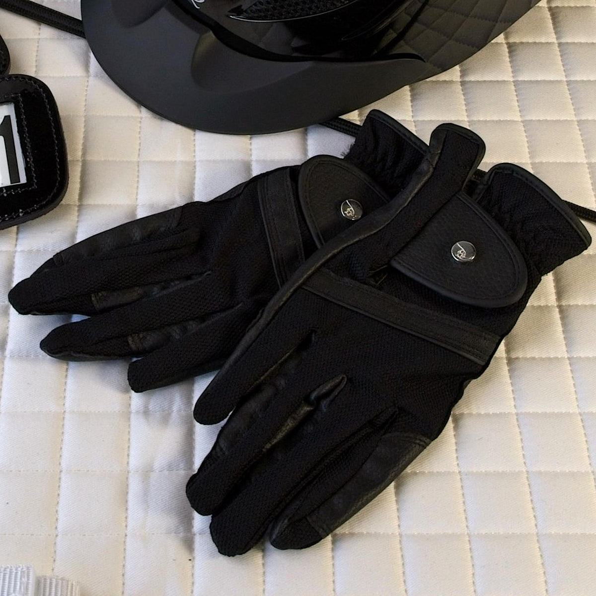 Pair of black riding gloves with leather details and subtly shiny buttons.