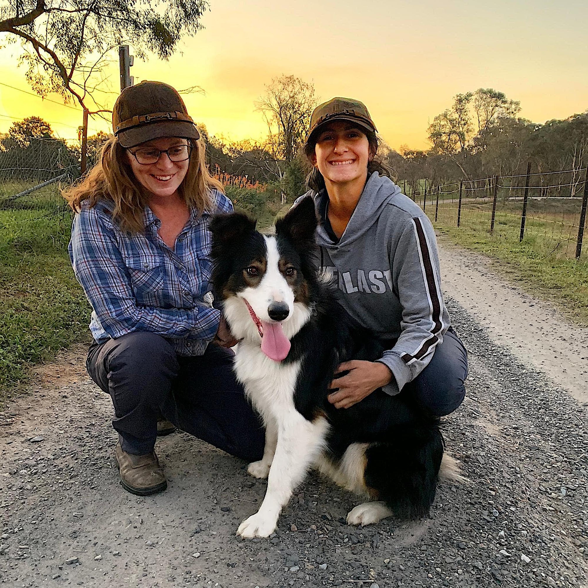 Two women wearing Equestrian cap, smiling while patting a dog.