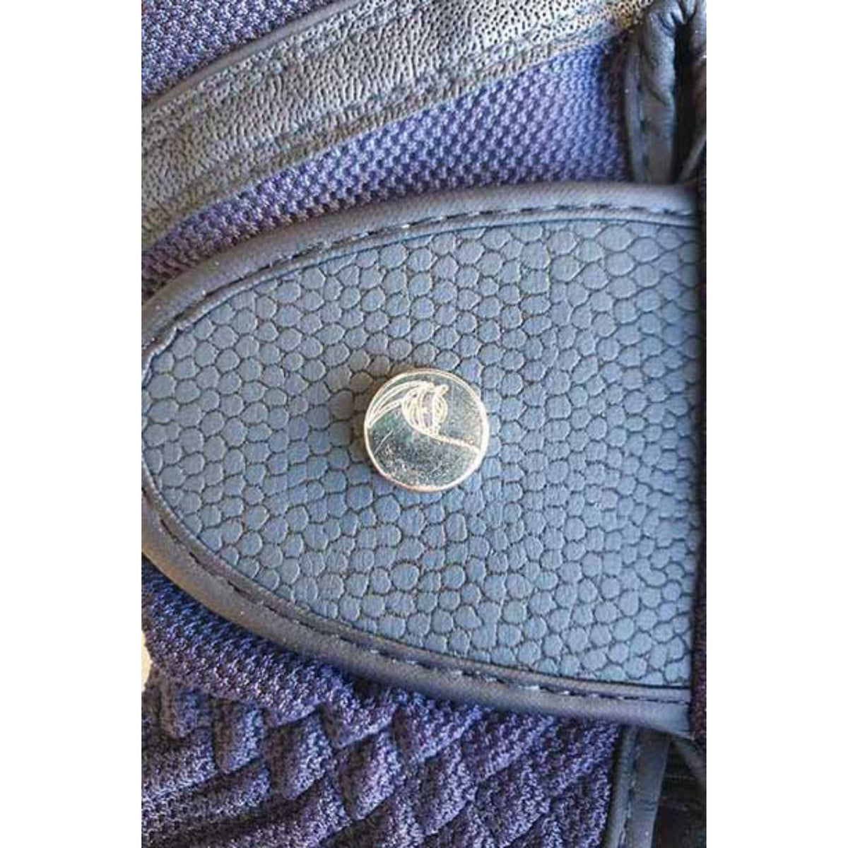 Close up of glove tab with silver button, with horse outline detail.